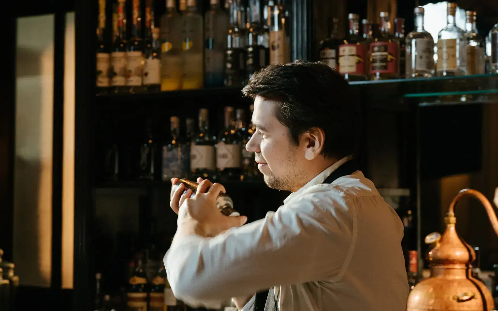 Bartender shaking a cocktail in front of a liquor shelf
