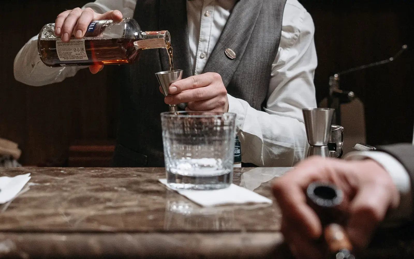 Bartender pouring a measured whiskey shot into a jigger at the bar