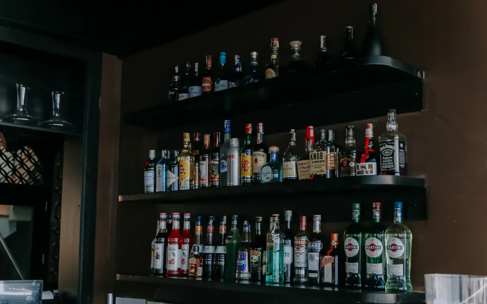Liquor bottles arranged on three black bar shelves