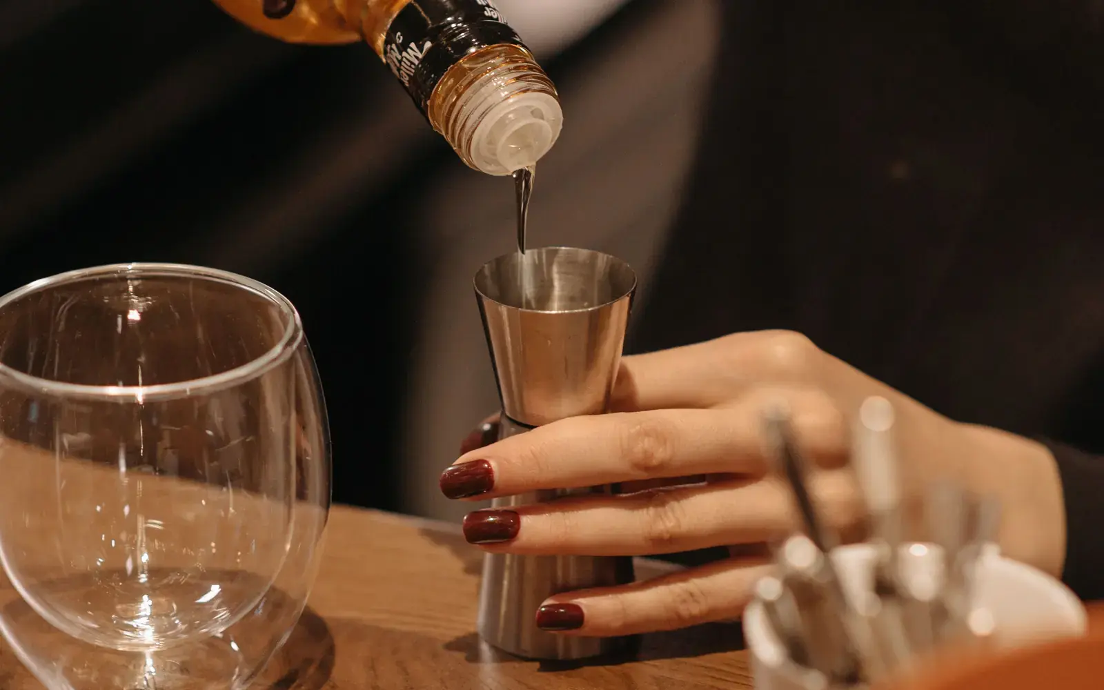Hand pouring a spirit from a bottle into a stainless jigger